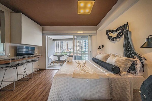 A modern bedroom with a large bed, a desk with a computer, and a view of the city through large windows. - Mode Perdizes (São Paulo)