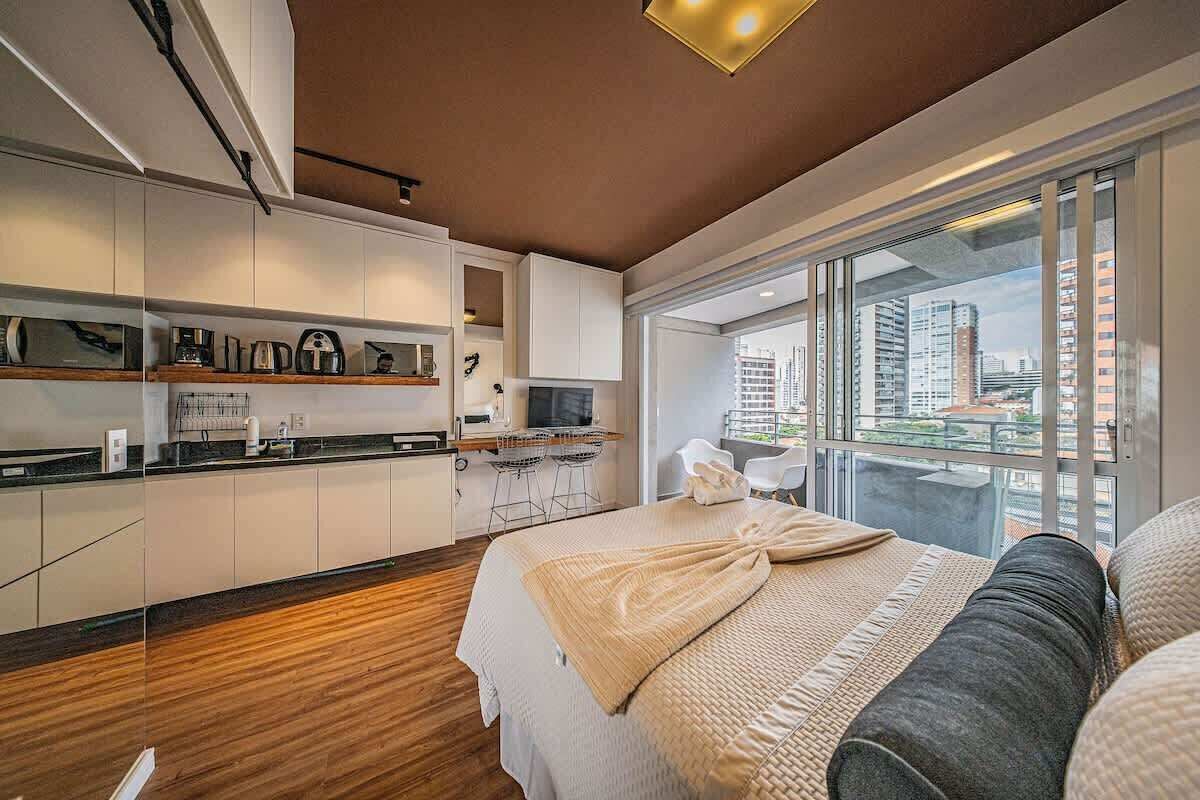 Une chambre d’hôtel moderne dotée d’un grand lit, d’une kitchenette et offrant une vue sur le paysage urbain.