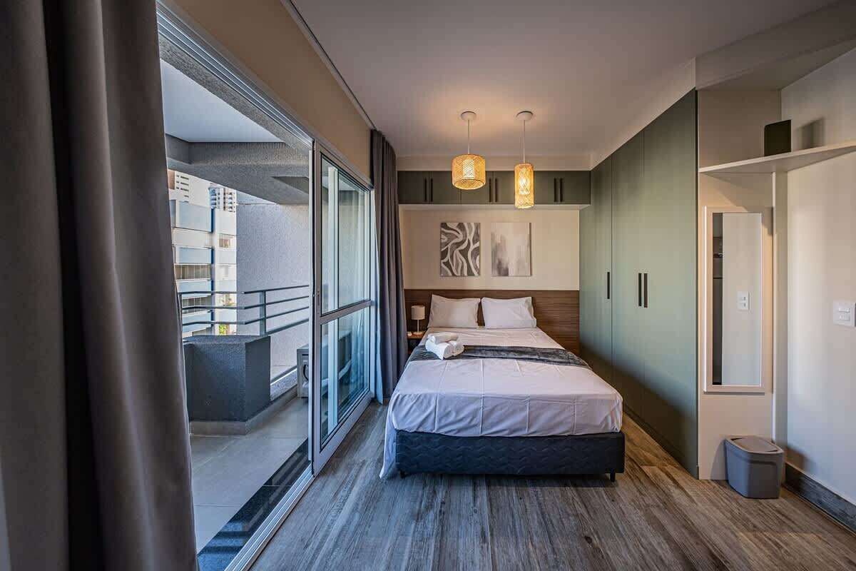 Habitación de hotel moderna con una cama grande, vistas a un balcón exterior por una puerta corredera e iluminación colgante.
