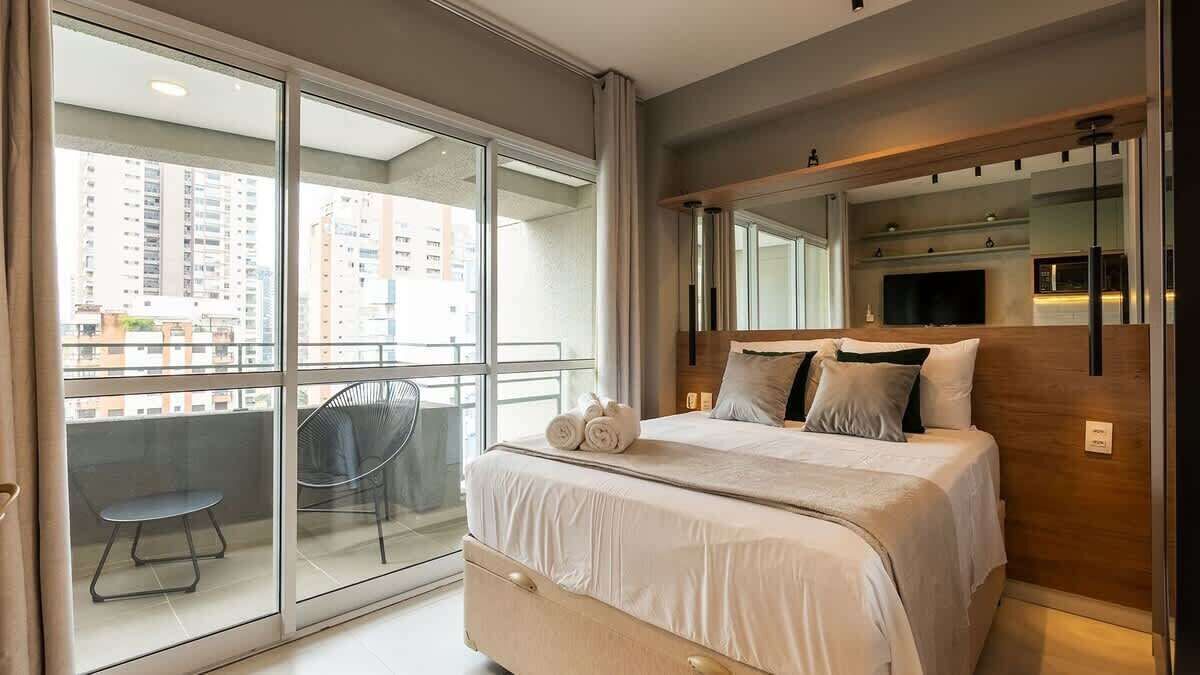 Un dormitorio moderno con una cama grande, un balcón con una silla y un televisor montado en la pared.