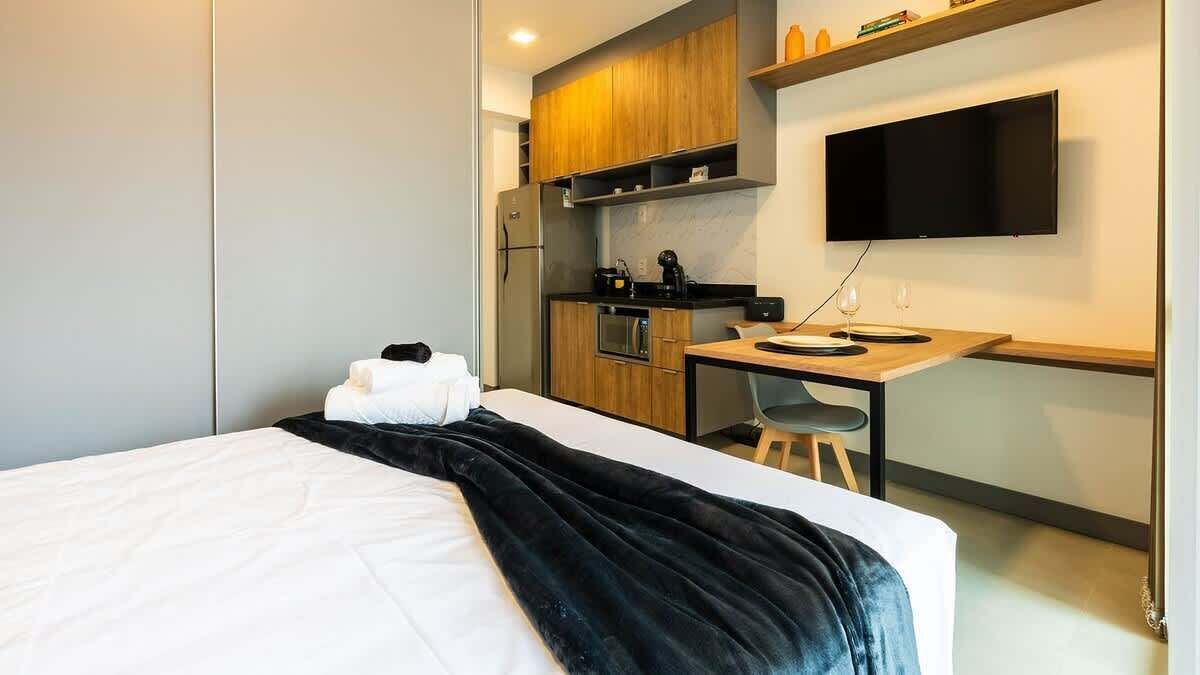 A hotel room with a bed, a desk, a kitchenette, and a TV.