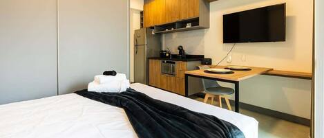 A hotel room with a bed, a desk, a kitchenette, and a TV.