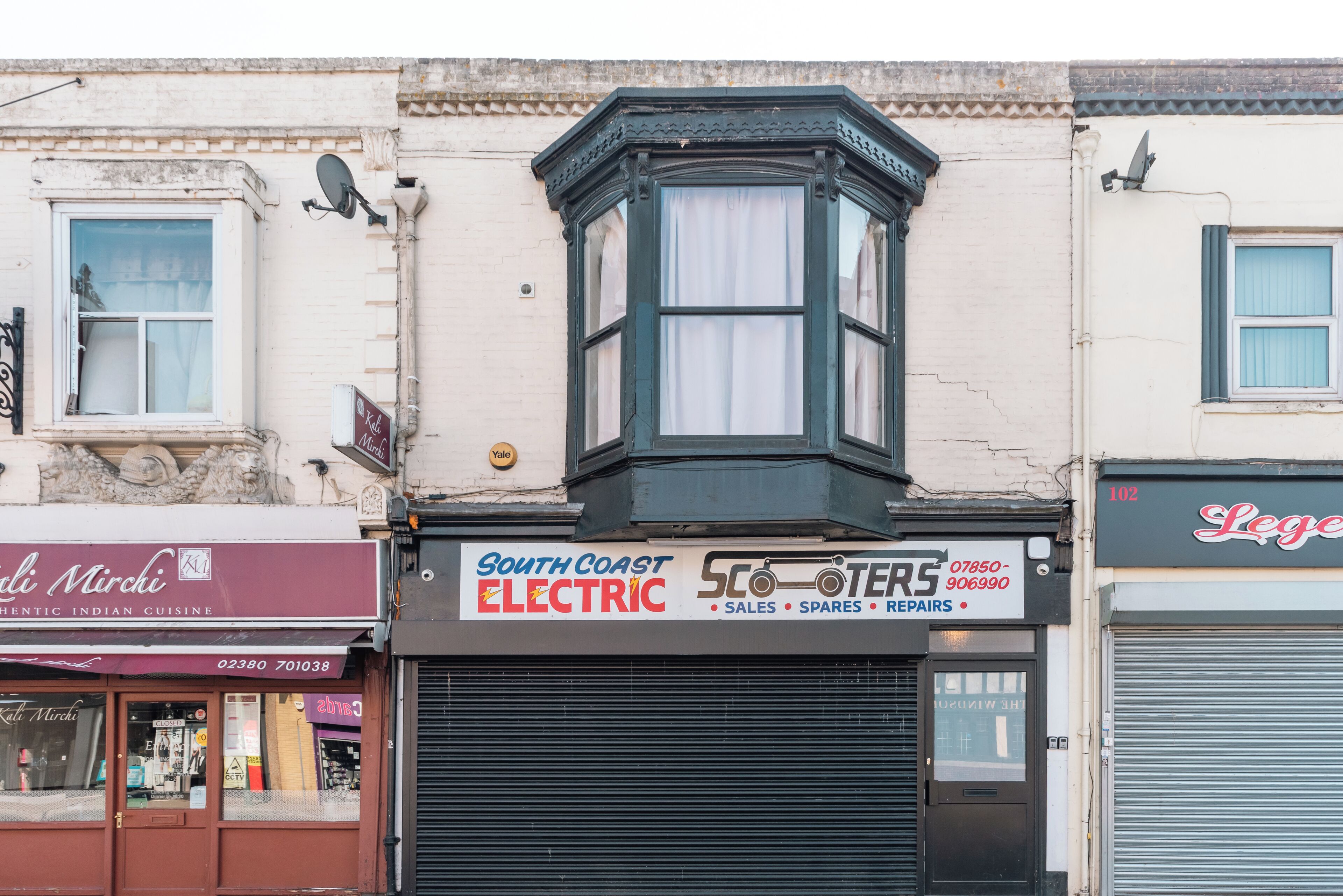 A corner building with a bay window, a closed shuttered shop, and a sign for 'South Coast Electric'.
