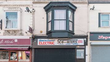 A corner building with a bay window, a closed shuttered shop, and a sign for 'South Coast Electric'.