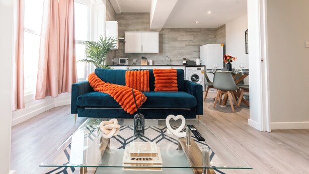 A modern living room with a blue sofa, glass coffee table, and a kitchen in the background. - Cozy 3-Bed Central Southampton (Shirley)