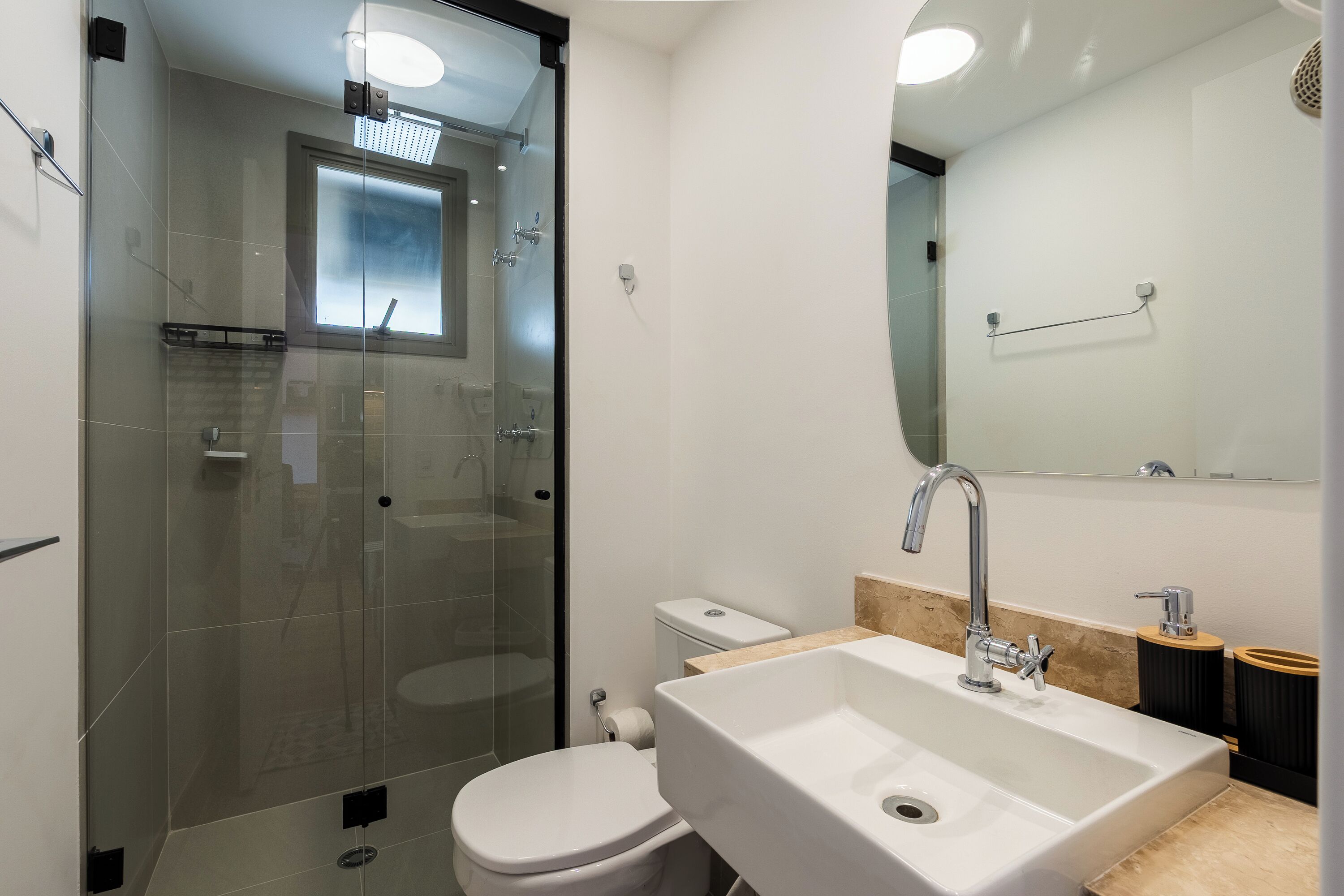 Une salle de bain moderne avec une douche à parois de verre, des toilettes blanches et un lavabo surmonté d’un miroir.