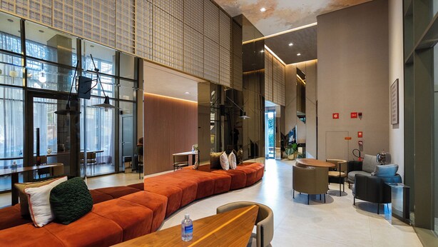 Un interior moderno con un sofá naranja largo, mesas de madera y una pared de vidrio con diseño de cuadrícula.