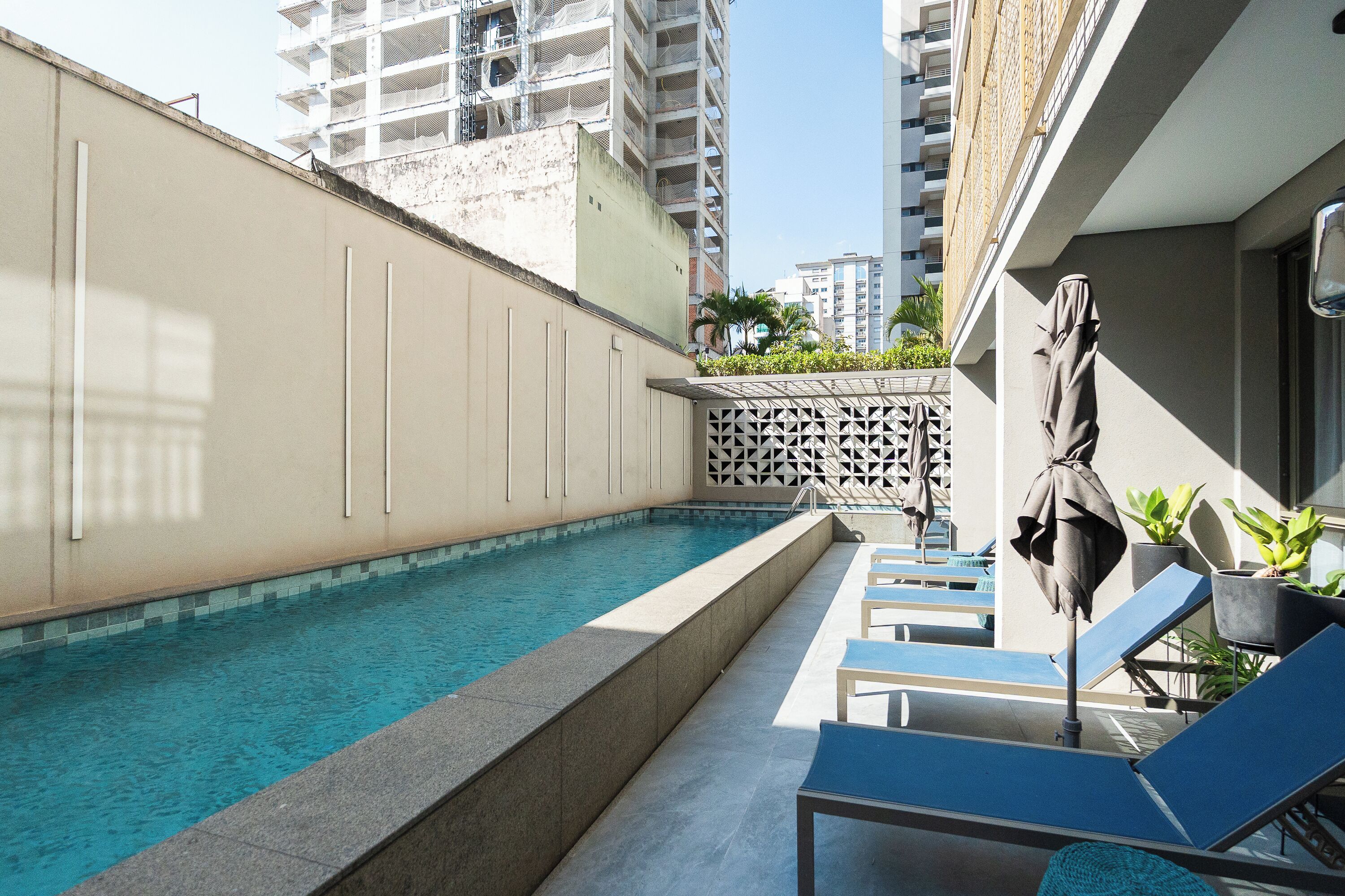 Une piscine entourée d’immeubles de grande hauteur, avec des chaises longues et des parasols.