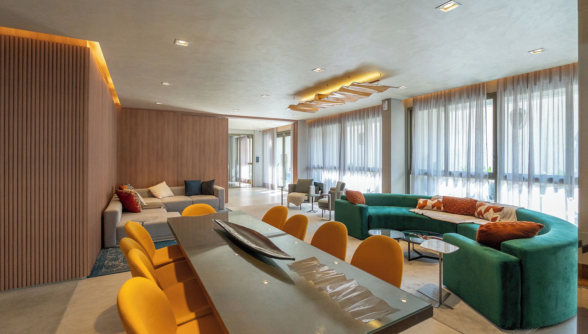A modern hotel lobby with a long dining table, yellow chairs, a green sofa, and large windows with sheer curtains.