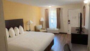 A hotel room with a large bed, a desk, a chair, a lamp, and a window with curtains. - Arab Knights Inn (Arab)