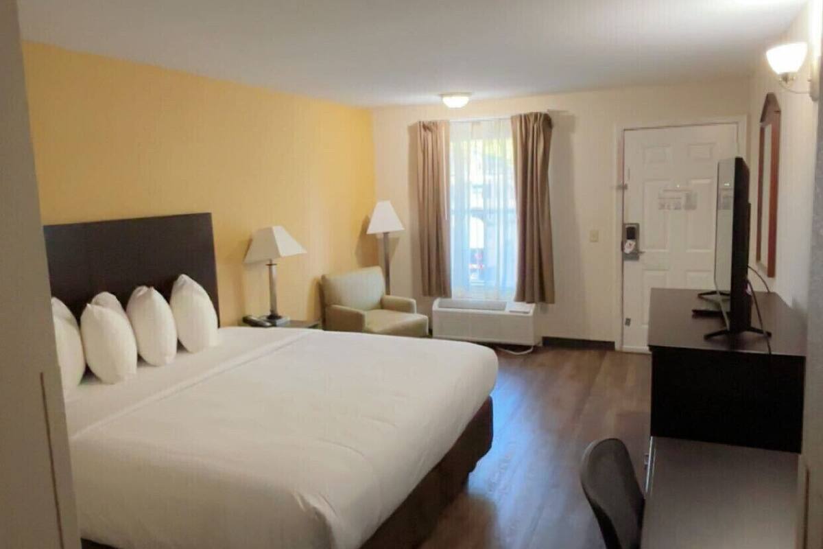 A hotel room with a large bed, a desk, a chair, a lamp, and a window with curtains.