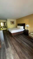 Una habitación de hotel con una cama, un escritorio, una silla, una lámpara y un cuadro en la pared.