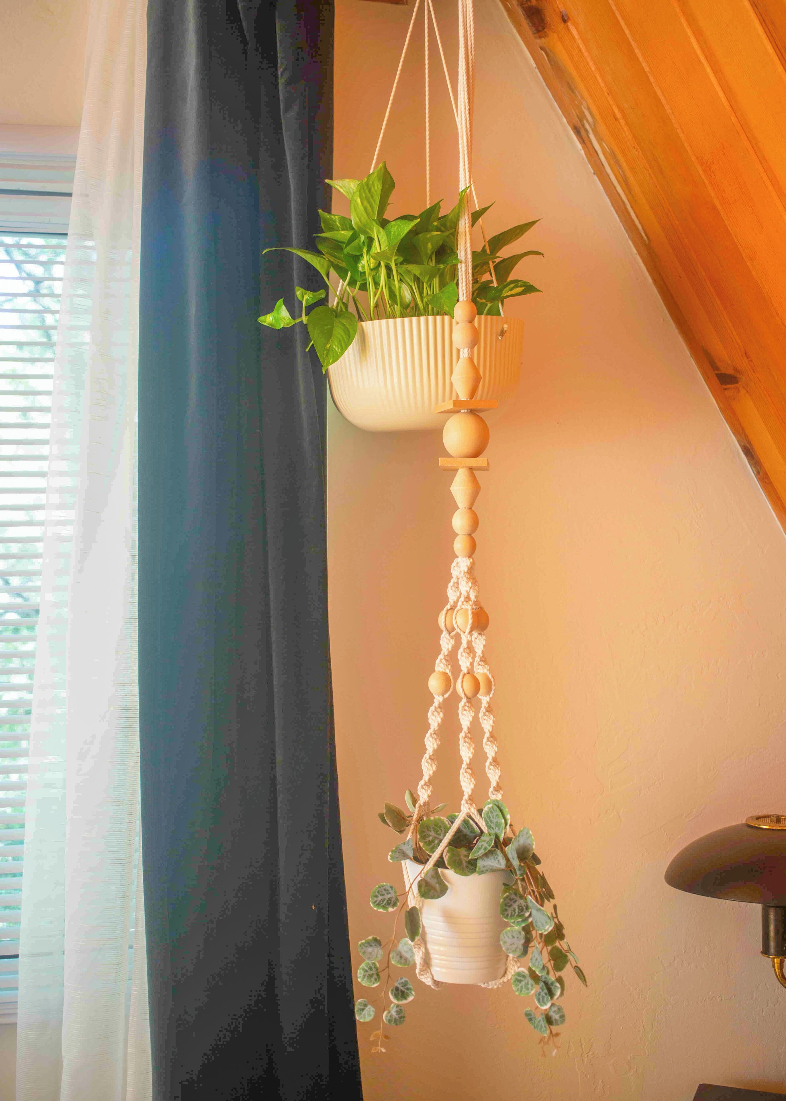 A room with a wooden ceiling, a hanging macrame plant holder with a plant, and a window with blinds.