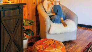 A cozy room with wooden walls, a cushioned chair, a lamp, and framed artwork. - La Forêt Retreat, Hiking, Lakes, Dog Friendly! (Running Springs)