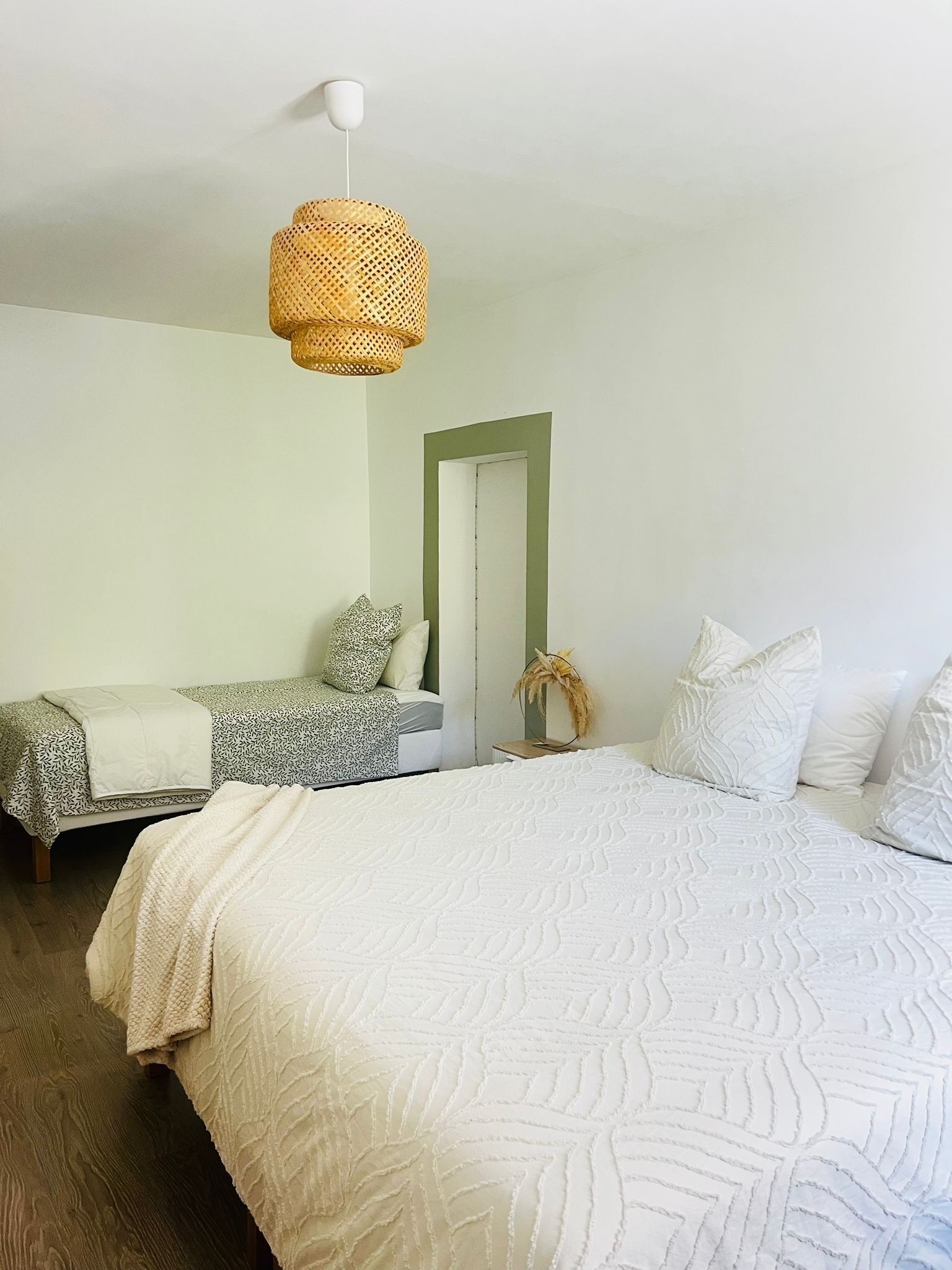 Une chambre avec un grand lit, un plus petit lit, un luminaire suspendu et une porte dotée d’un cadre vert.