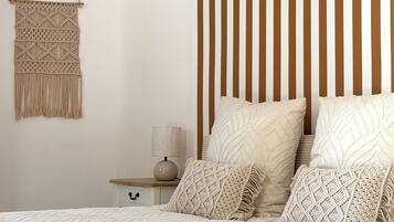 Una camera da letto con un letto, cuscini, un comodino, una lampada e un decoro macramè a parete.