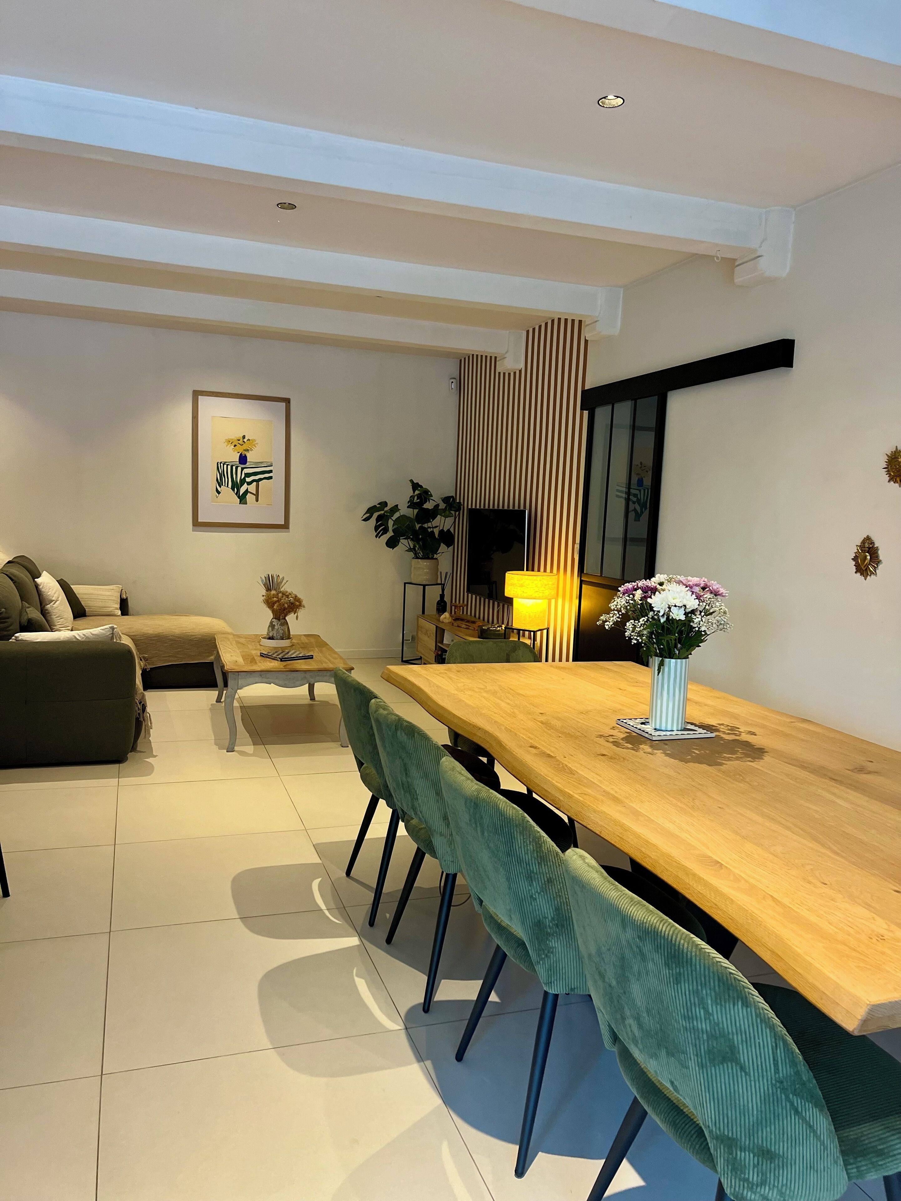 Un salon moderne avec une table à manger en bois, des chaises à l’assise verte, un canapé et une œuvre d’art encadrée accrochée au mur.