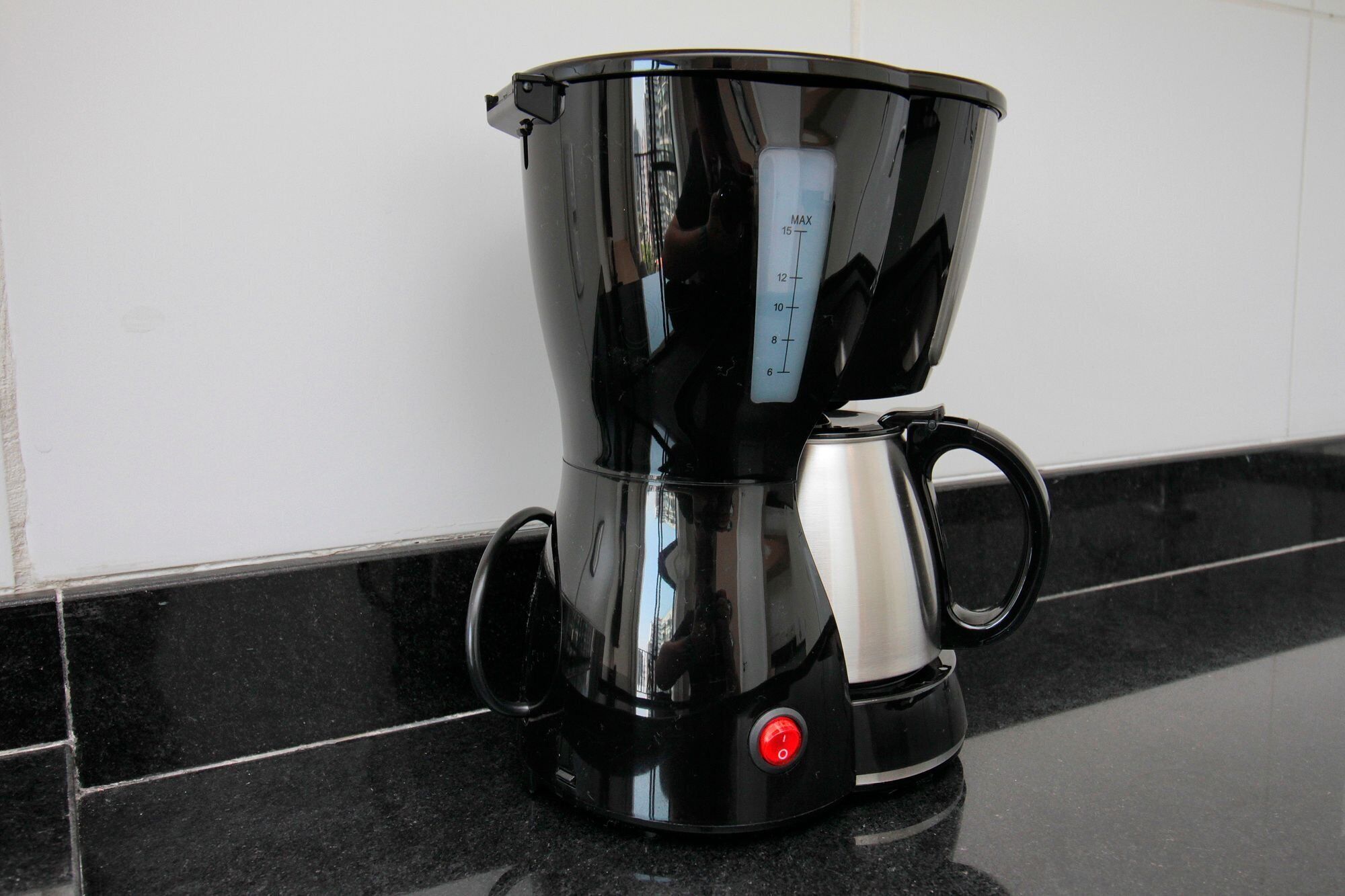 A black coffee maker with a digital scale on the side, placed on a black tiled countertop.