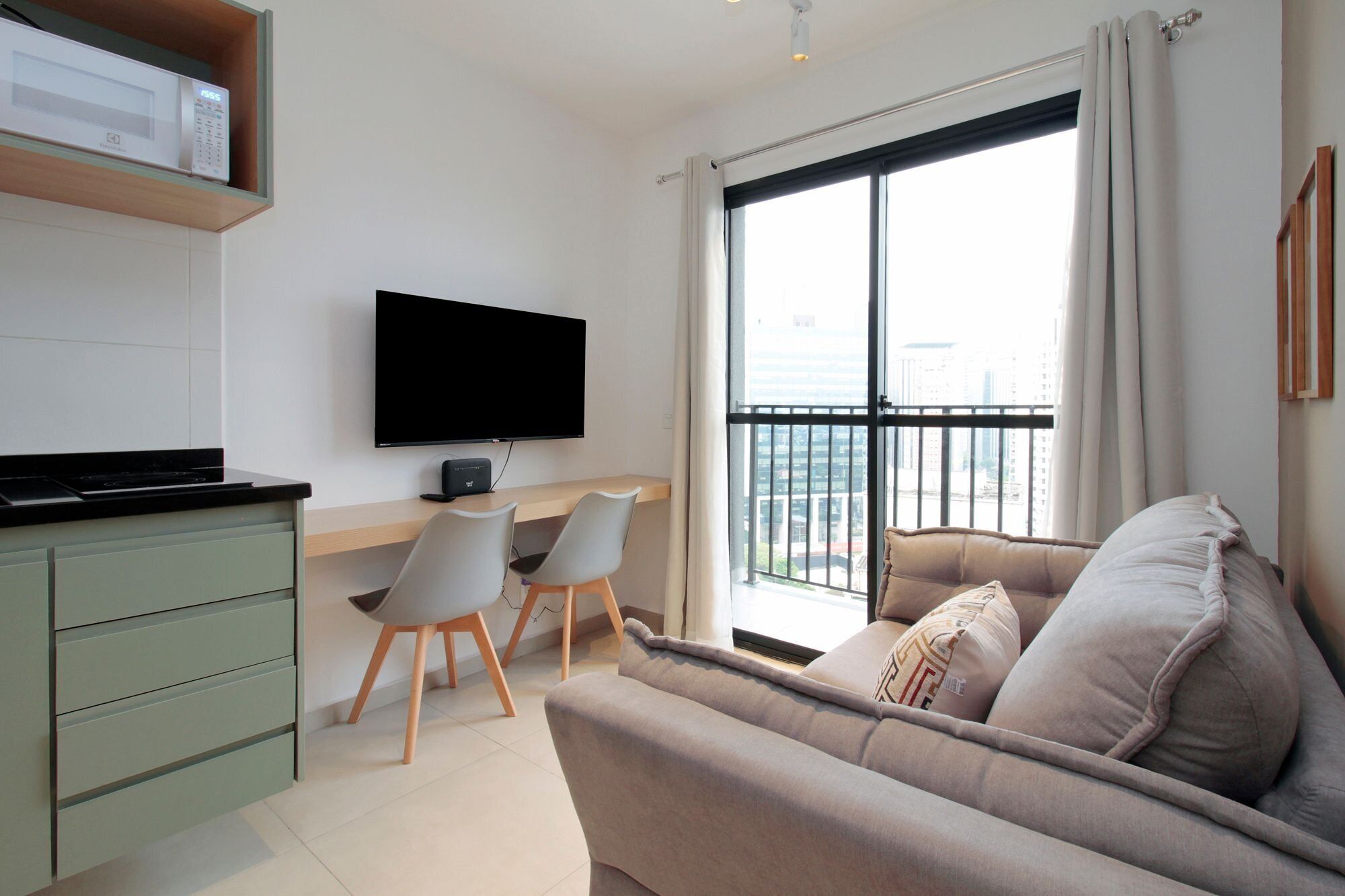 A modern living room with a sofa, a flat-screen TV, a dining table with chairs, and a kitchen area with a microwave.