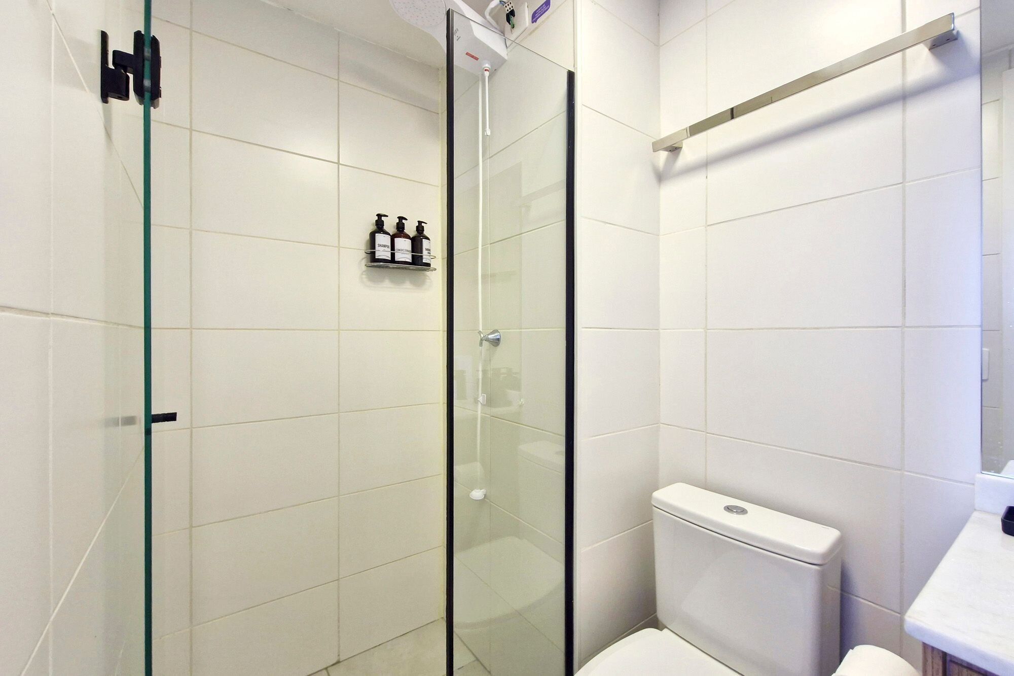 A modern bathroom with a glass shower enclosure, white tiles, and a toilet.