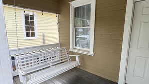 Un porche con un banco de madera blanco, una puerta blanca y una ventana que ofrece vistas a un vehículo.