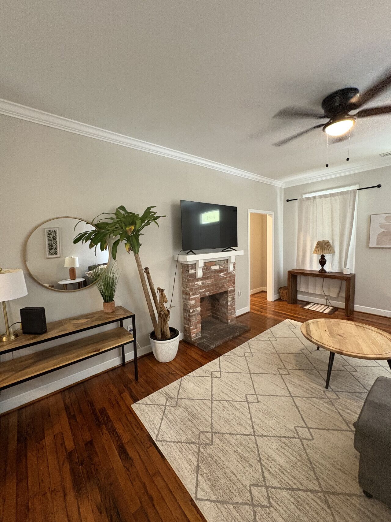Ein Wohnzimmer mit Kamin aus Backstein, Flachbildfernseher, Deckenventilator und Couchtisch aus Holz.