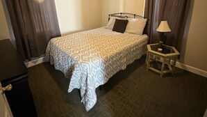 Un dormitorio con cama, escritorio, lámpara y ventilador de techo.