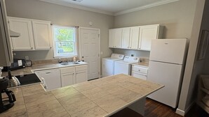 Una cocina compacta con armarios blancos, horno integrado, refrigerador y cafetera.