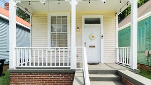 A porch with white railings, a brick base, and a white door with a doormat. - Sun cottage near downtown (Columbus)