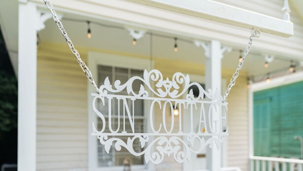 A white sign with ornate designs hanging from a porch railing, reading "SUN COTTAGE." - Sun cottage near downtown (Columbus)