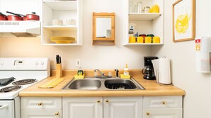 A kitchen with white cabinets, a double sink, a stove, and various kitchen items. - Sun cottage near downtown (Columbus)