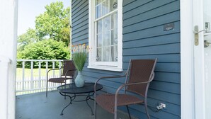 A porch with a round table and two wicker chairs, a vase with greenery, and a white picket fence. - Sky cottage near downtown (Columbus)