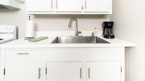 A kitchen with white cabinets, a stainless steel sink, a coffee maker, and a green towel on the counter. - Apple cottage near downtown (Columbus)