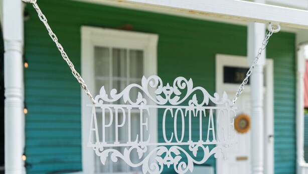 A white sign with "APPLE COTTAGE" written on it, hanging from a white porch railing. - Apple cottage near downtown (Columbus)