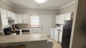 A kitchen with white cabinets, a large island with stools, a refrigerator, and a dishwasher. - Oak Bungalow in Midtown (Columbus)