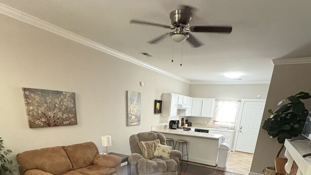 A living room with a brown sofa, a coffee table, and a patterned rug. There is a ceiling fan, a kitchen in the background, and a brick fireplace. - Oak Bungalow in Midtown (Columbus)