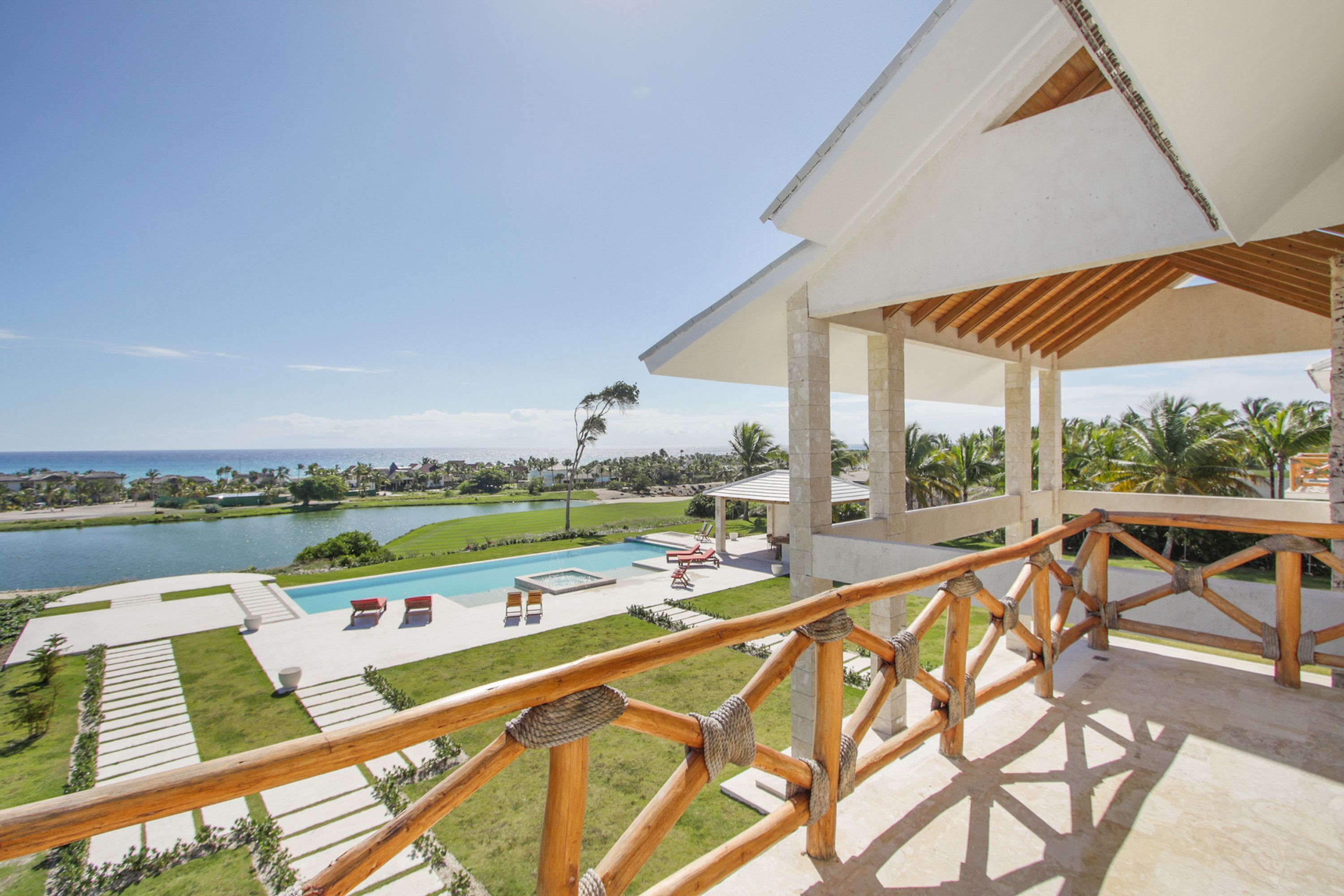 Un área de piscina con vista al océano, un porche cubierto y un césped bien cuidado.