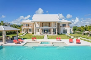 A two-story house with a swimming pool, red lounge chairs, and a well-maintained lawn. - Stunning 6BR Villa With Ocean View in Cap Cana (Punta Cana)