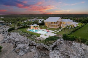 A large, modern house with a swimming pool, surrounded by lush greenery and rocky terrain. - Stunning 6BR Villa With Ocean View in Cap Cana (Punta Cana)
