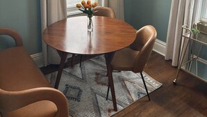 A dining area with a round wooden table, two chairs, a vase with flowers, and a modern light fixture. - Boutique Studio Apartment (La Porte)