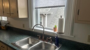 A kitchen with a double sink, a window with blinds, and a potted plant on the windowsill.