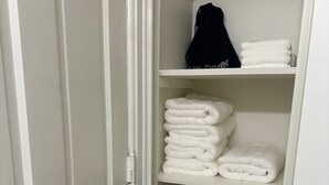 Un armario con estantes blancos, una bolsa colgada y toallas dobladas.