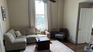 Una sala de estar con sofá, mesa de centro, alfombra, sillón y ventana con cortinas.