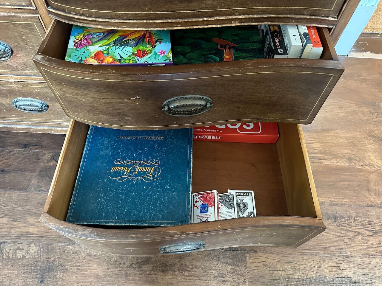 Eine Holzkiste mit einem blauen Buch mit dem Titel 'Scrabble' und Spielkarten.