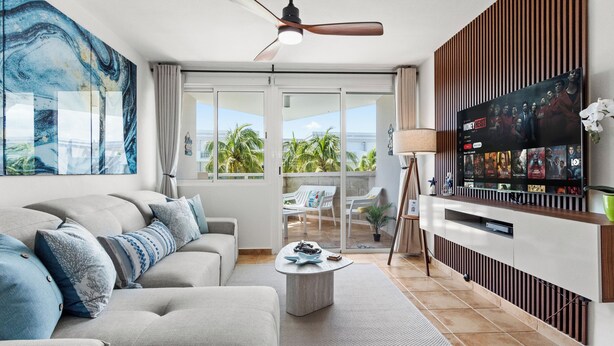 A modern living room with a sofa, coffee table, and a flat-screen TV mounted on a wooden panel. - Charming Beachfront Retreat - Wake Up to Waves - 2 BD Apt with AC at Río Grande (Río Grande)