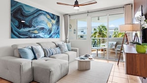 A modern living room with a grey sectional sofa, a round coffee table, and a large abstract painting on the wall. - Charming Beachfront Retreat - Wake Up to Waves - 2 BD Apt with AC at Río Grande (Río Grande)
