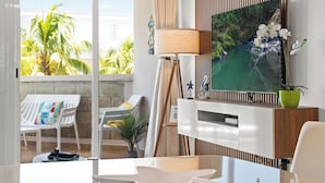 A modern living room with a large window, a floor lamp, a TV, and a small table. - Charming Beachfront Retreat - Wake Up to Waves - 2 BD Apt with AC at Río Grande (Río Grande)