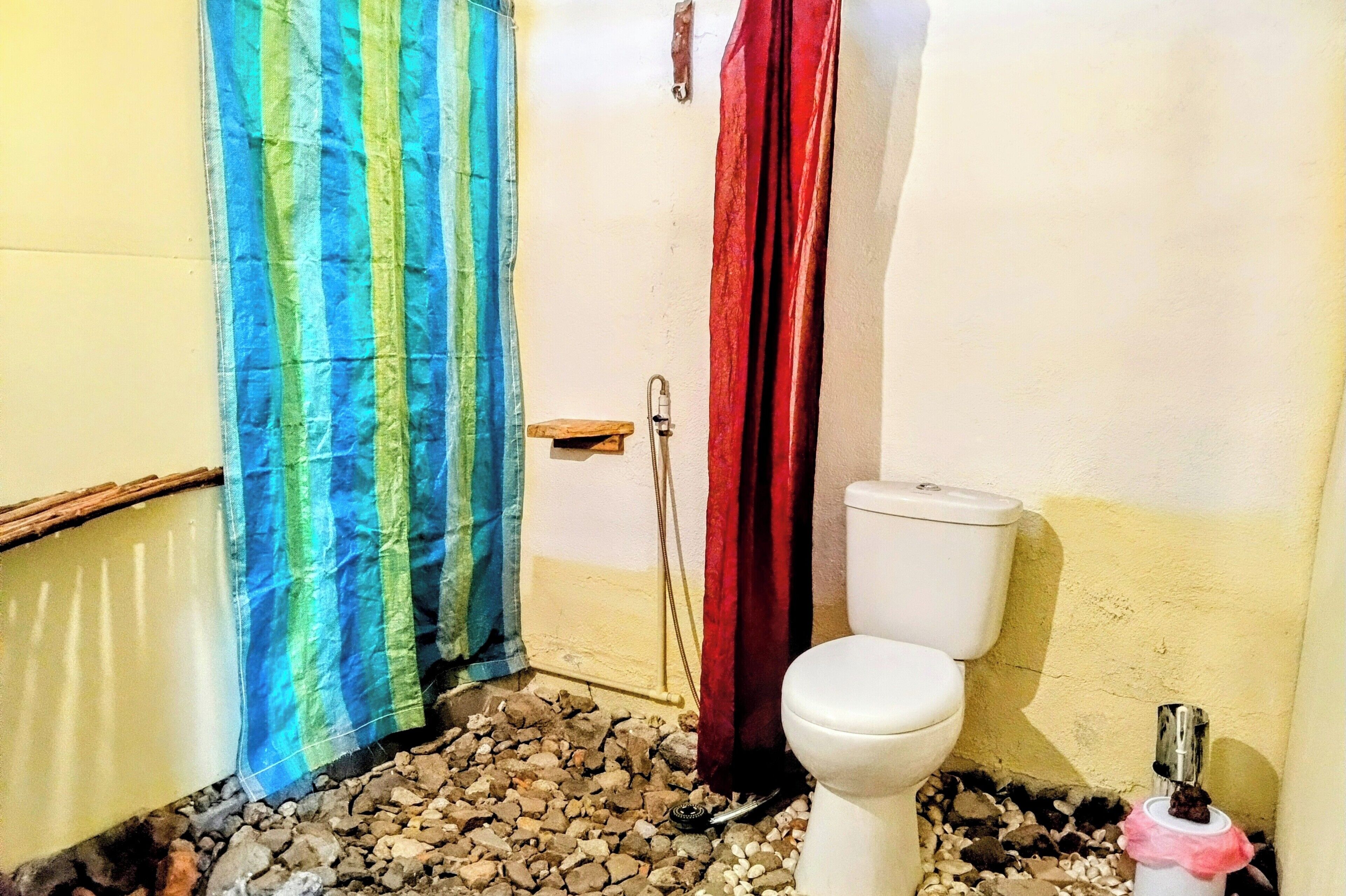 A bathroom with a toilet, a shower curtain, and a small stool.