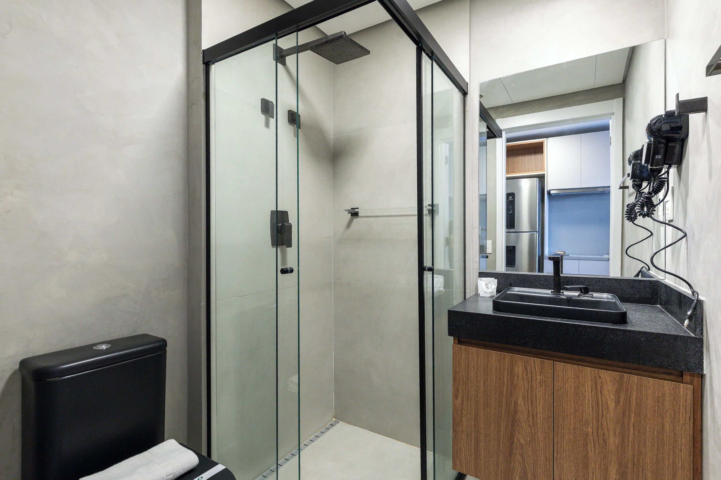 Un baño moderno con cabina de ducha de vidrio, inodoro negro y tocador de madera con lavamanos.