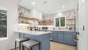 Een moderne keuken met een centraal eiland, barkrukken, houten planken en een raam met uitzicht op bomen.